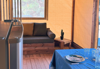Interieur van een safaritent met bank, tafel, cactus en gedekte eettafel bij Flower Camping La Plage, Frankrijk.