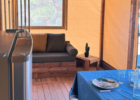 Indretning af en safaritelt med sofa, bord, kaktus og dækket spisebord på Flower Camping La Plage i Frankrig.