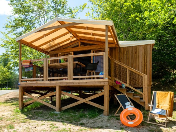 Outdoor wooden lodge at Cosyflower Premium with open veranda, deck chairs, and an orange pool float.