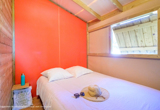 Helles Schlafzimmer in der Cosyflower Premium Lodge mit Doppelbett, Strohhut und Sonnenbrille auf dem Bett.