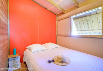 Lichte slaapkamer in de Cosyflower Premium lodge met tweepersoonsbed, strohoed en zonnebril op het bed.