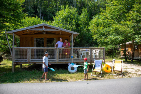 Twee kinderen spelen voor een Sweetflower Premium safaritent, terwijl twee volwassenen op het terras staan.