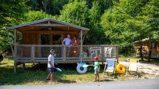 Due bambini giocano davanti a una tenda safari Sweetflower Premium mentre due adulti osservano dalla veranda.