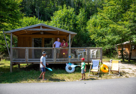 Twee kinderen spelen voor een Sweetflower Premium safaritent, terwijl twee volwassenen op het terras staan.