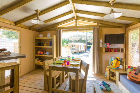 Sfeervolle glamping accommodatie met houten tafel, zithoek, decoratie en zicht op de natuur buiten.