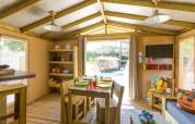 Alojamiento glamping acogedor con muebles de madera, comedor interior y vista hacia la naturaleza.
