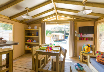 Sfeervolle glamping accommodatie met houten tafel, zithoek, decoratie en zicht op de natuur buiten.