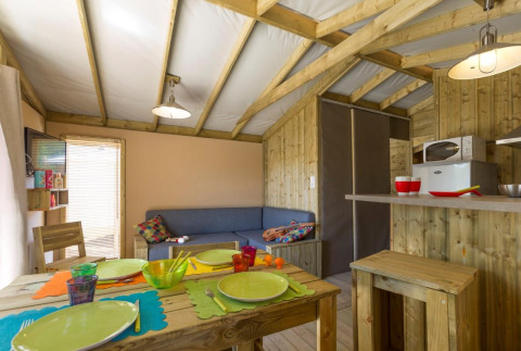 Gezellig glamping-interieur met houten tafel, vrolijk servies en een kleine, goed uitgeruste kitchenette.