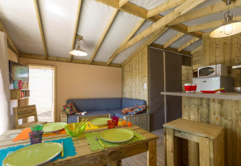Gezellig glamping-interieur met houten tafel, vrolijk servies en een kleine, goed uitgeruste kitchenette.