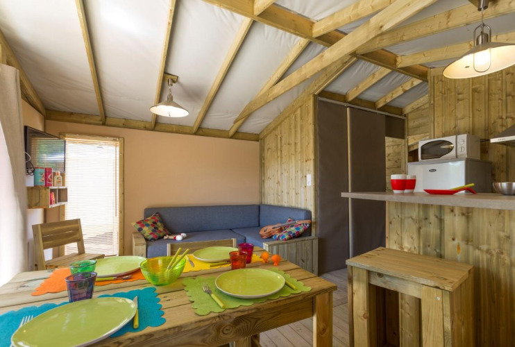 Intérieur de cabane glamping cosy avec meubles en bois, vaisselle colorée et petite kitchenette équipée.
