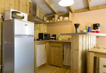 Coin cuisine de glamping chaleureux en bois avec frigo, micro-ondes, bar et étagères ouvertes.