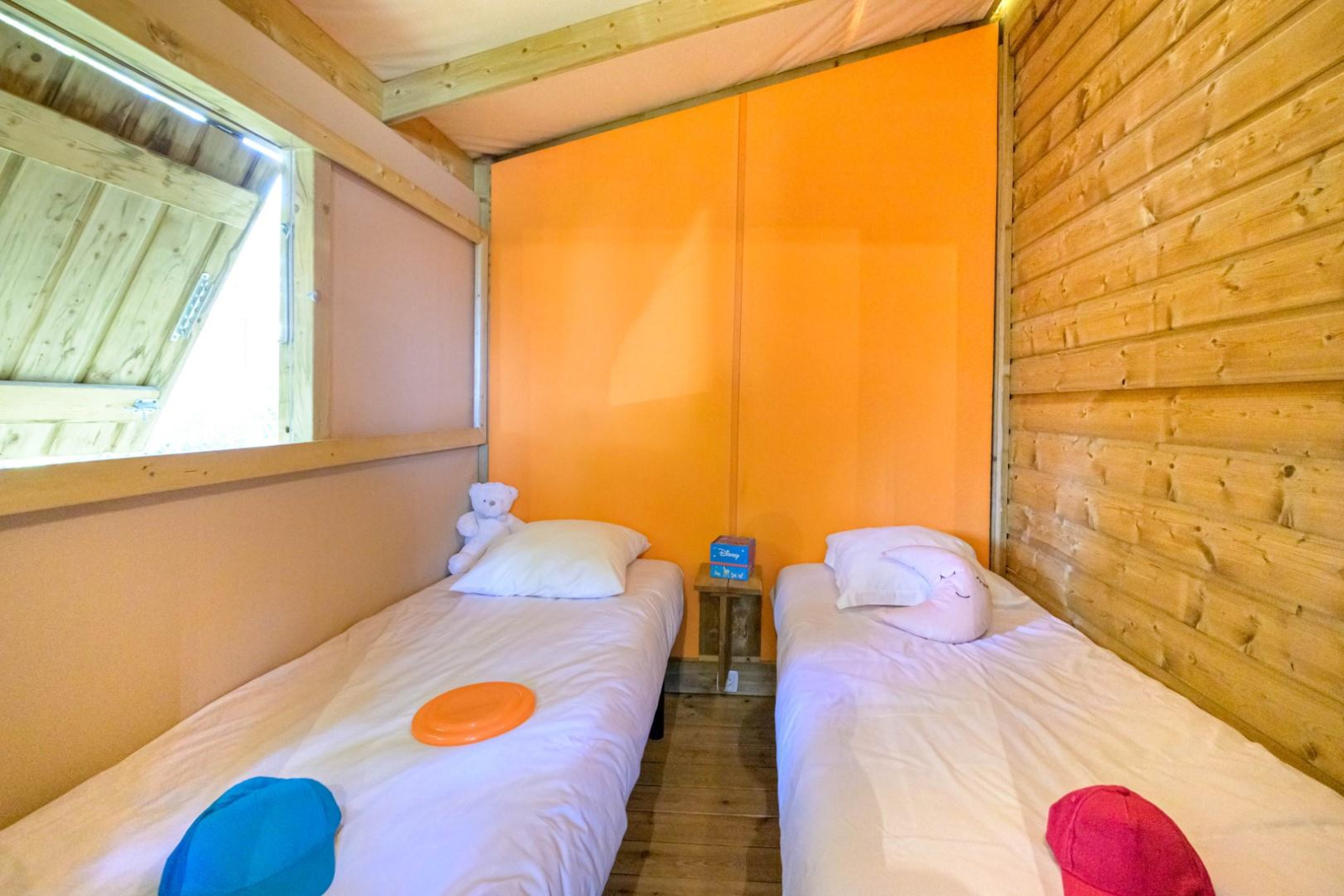 Twee eenpersoonsbedden in een knusse glampingaccommodatie met houten wanden en kleurrijke kussens.