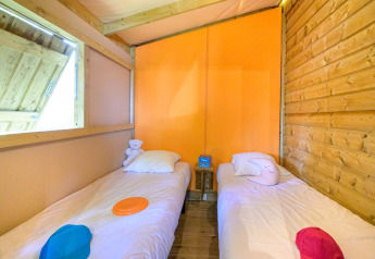 Twee éénpersoonsbedden in een gezellige glampinghut met houten panelen en kleurrijke accessoires.