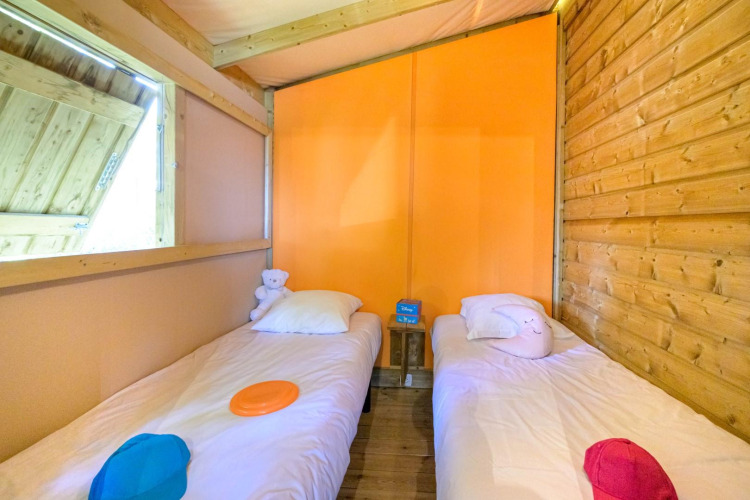 Deux lits une place dans une tente de glamping chaleureuse, ornée de bois, coussins colorés et peluches.