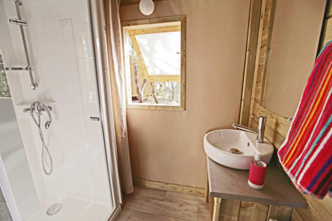 Badezimmer einer Glamping-Unterkunft mit Dusche, Waschbecken, Fenster und buntem Handtuch.