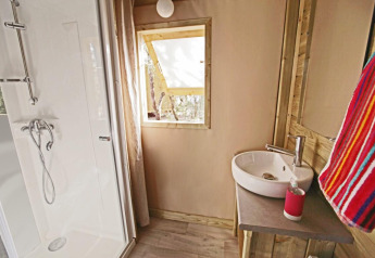 Baño en alojamiento glamping con ducha, lavabo, ventana y toalla de colores brillantes visible.