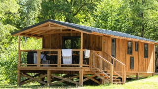 En VIP Premium Lodge i træ omgivet af grønne træer, med en veranda og trapper i solrigt skovområde.