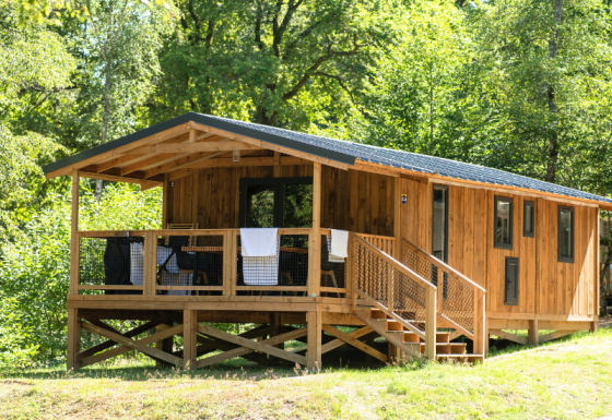 En VIP Premium Lodge i træ omgivet af grønne træer, med en veranda og trapper i solrigt skovområde.