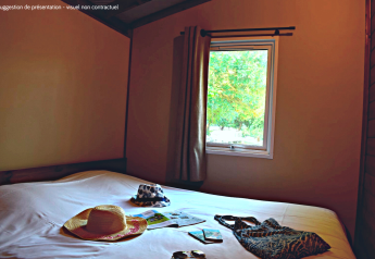 Camera nella VIP Premium Lodge a Flower Camping La Plage, Francia, con cappelli e accessori estivi sul letto.