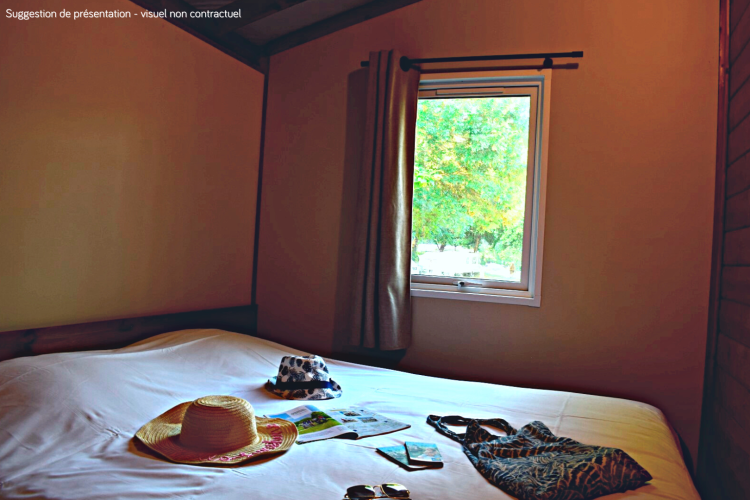 Camera nella VIP Premium Lodge a Flower Camping La Plage, Francia, con cappelli e accessori estivi sul letto.