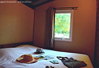 Soveværelse i VIP Premium Lodge på Flower Camping La Plage, Frankrig, med hatte og sommerudstyr på sengen.