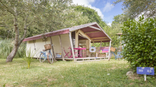 Tenda safari Freeflower Standard con biciclette e arredi colorati all'aperto tra gli alberi e il verde.