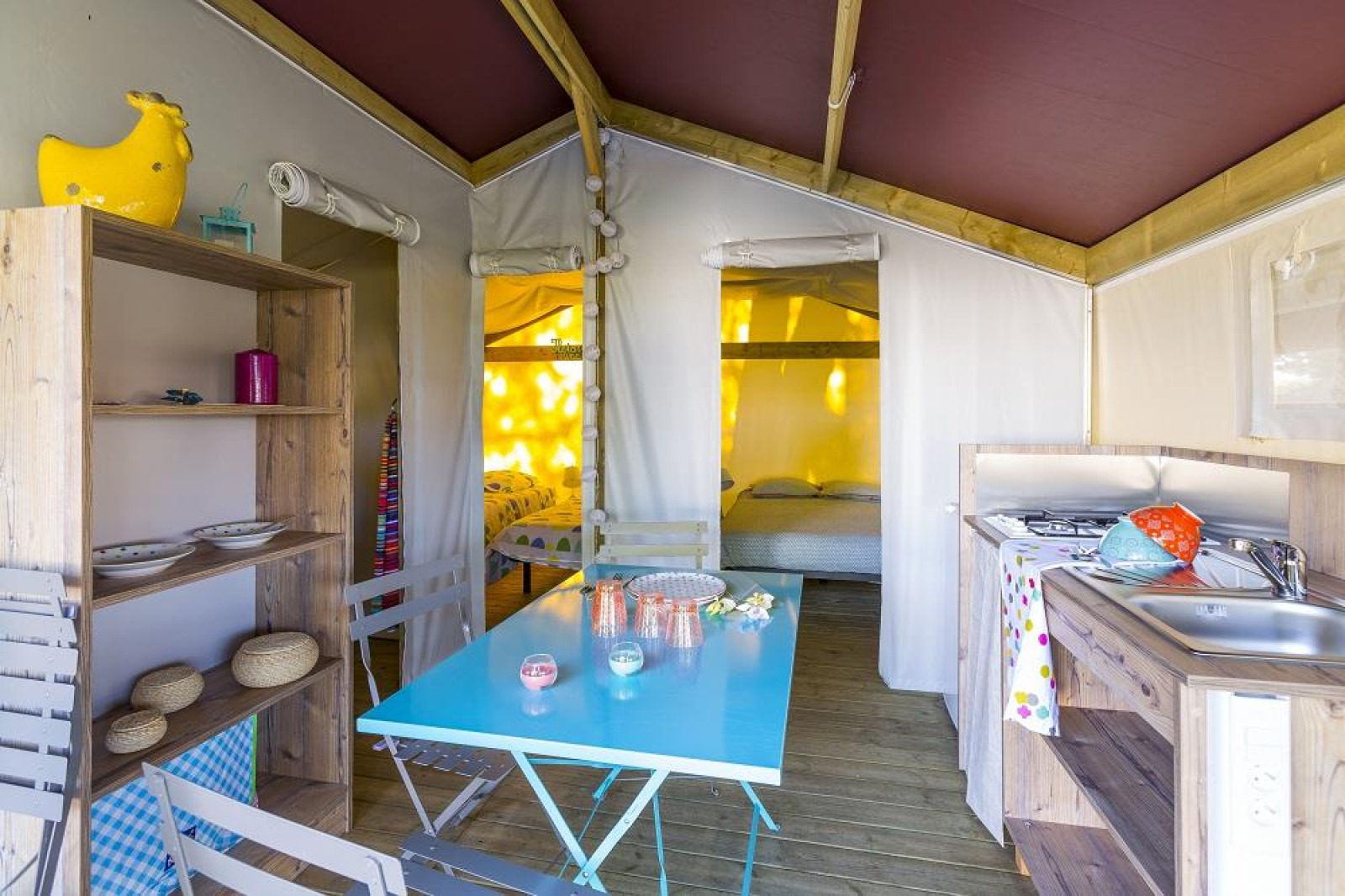 Interieur van een safaritent met eettafel, keuken en bedden bij Flower Camping Cap Finistère, Frankrijk.