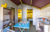 Binnenkant van een safaritent met eetplaats, keuken en bedden bij Flower Camping Cap Finistère, Frankrijk.