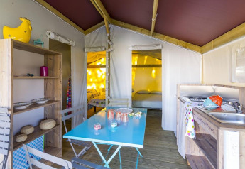 Interno di tenda safari con tavolo da pranzo, cucina e letti presso Flower Camping Cap Finistère, Francia.