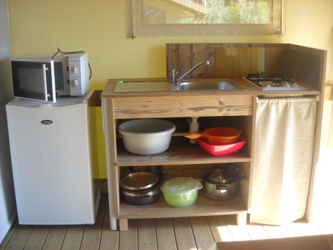 Kleine keuken in een safaritent met koelkast, magnetron, gootsteen, kookplaten en keukengerei zichtbaar.