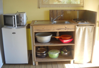 Kleine keuken in een safaritent met koelkast, magnetron, gootsteen, kookplaten en keukengerei zichtbaar.