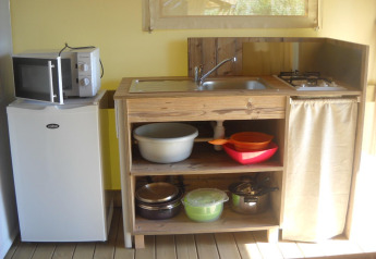 Piccola cucina in una tenda safari con frigorifero, microonde, lavello, fornello e utensili da cucina.