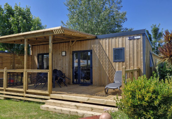Buitenaanzicht van een Homeflower premium lodge met houten terras, tuinmeubels en groene planten.