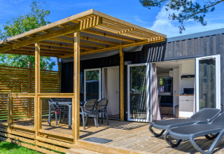 Terrazza all'aperto con lettini e tavolo da pranzo al lodge Homeflower premium presso Flower Camping Cap Finistère, Francia.