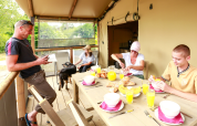 Familie beim Frühstück im Safari-Zelt mit Croissants, Saft und Hund im Flower Camping Le Vieux Moulin, Frankreich.