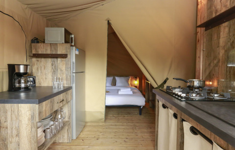 Vista interior de una tienda safari cómoda con cocina y dormitorio en Flower Camping Le Vieux Moulin, Francia.