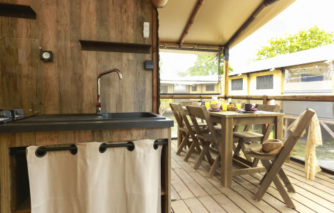 Interior of a safari tent with wooden furniture, dining area, and kitchen at Flower Camping Le Vieux Moulin.