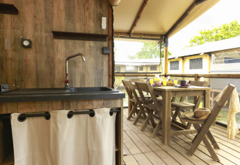 Interno di una tenda safari con arredi in legno, zona pranzo e cucina al Flower Camping Le Vieux Moulin.
