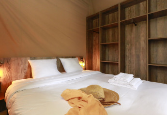 Letto accogliente con lenzuola bianche e scaffali in legno in una tenda safari al Flower Camping Le Vieux Moulin.