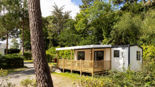Hébergement glamping Stacaravan Premium entouré d’arbres et de verdure sous un ciel bleu clair.