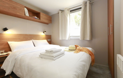 Camera glamping moderna con letto matrimoniale, dettagli in legno, finestra e tende chiare.