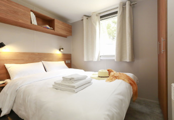 Chambre moderne d’hébergement glamping avec lit double, meubles en bois et fenêtre à rideaux clairs.