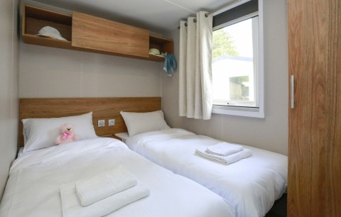 Stanza di glamping luminosa con due letti singoli, lenzuola bianche, finestra e mensole in legno.