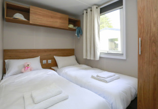 Ein helles Glamping-Zimmer mit zwei Einzelbetten, weißer Bettwäsche, Fenster und Wandregalen.