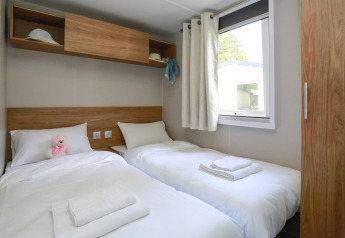 Stanza di glamping luminosa con due letti singoli, lenzuola bianche, finestra e mensole in legno.