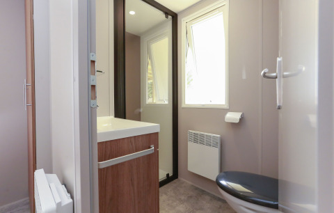 Salle de bains moderne dans un hébergement glamping avec fenêtre, toilettes, lavabo et miroir.