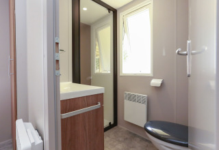 Baño moderno en alojamiento glamping con ventana, inodoro, lavabo, espejo y luz natural.