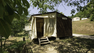 Vista exterior del lodge Canvas Mobile-Home Tithome, con revestimiento de madera y cortinas abiertas rodeado de árboles.