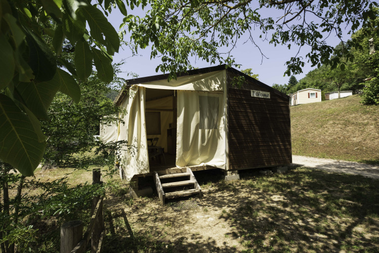 Exterior view of Canvas Mobile-Home Tithome lodge, with wood siding and open curtains in a leafy area.
