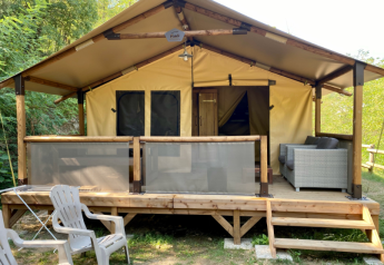 Safari tent genaamd Bali Safari Tent met overdekt terras, tuinbank en plastic stoelen in een bosrijke omgeving.